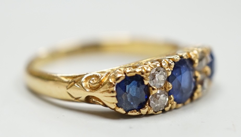 A late Victorian 18ct gold and three stone sapphire set ring, with four stone diamond set spacers, size M, gross weight 4.1 grams.